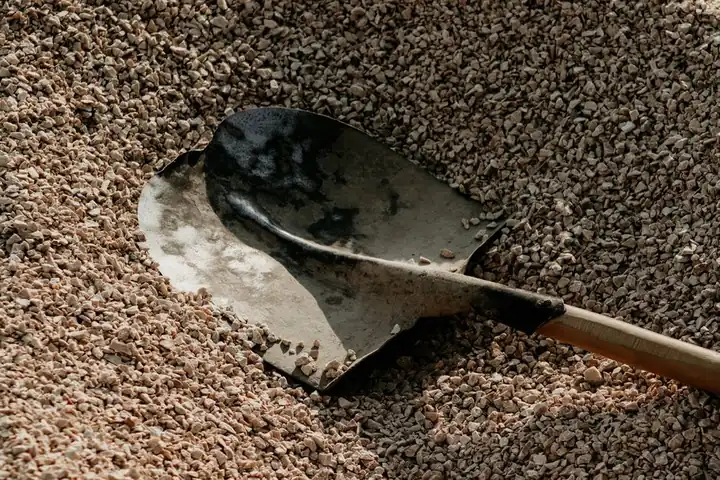 A metal shovel lying on a pile of small pebbles, suggesting outdoor landscaping or construction activities.